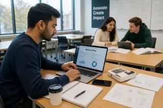Young adult student in a sunlit university classroom working on a laptop and prototype, with two other students collaborating in the background.